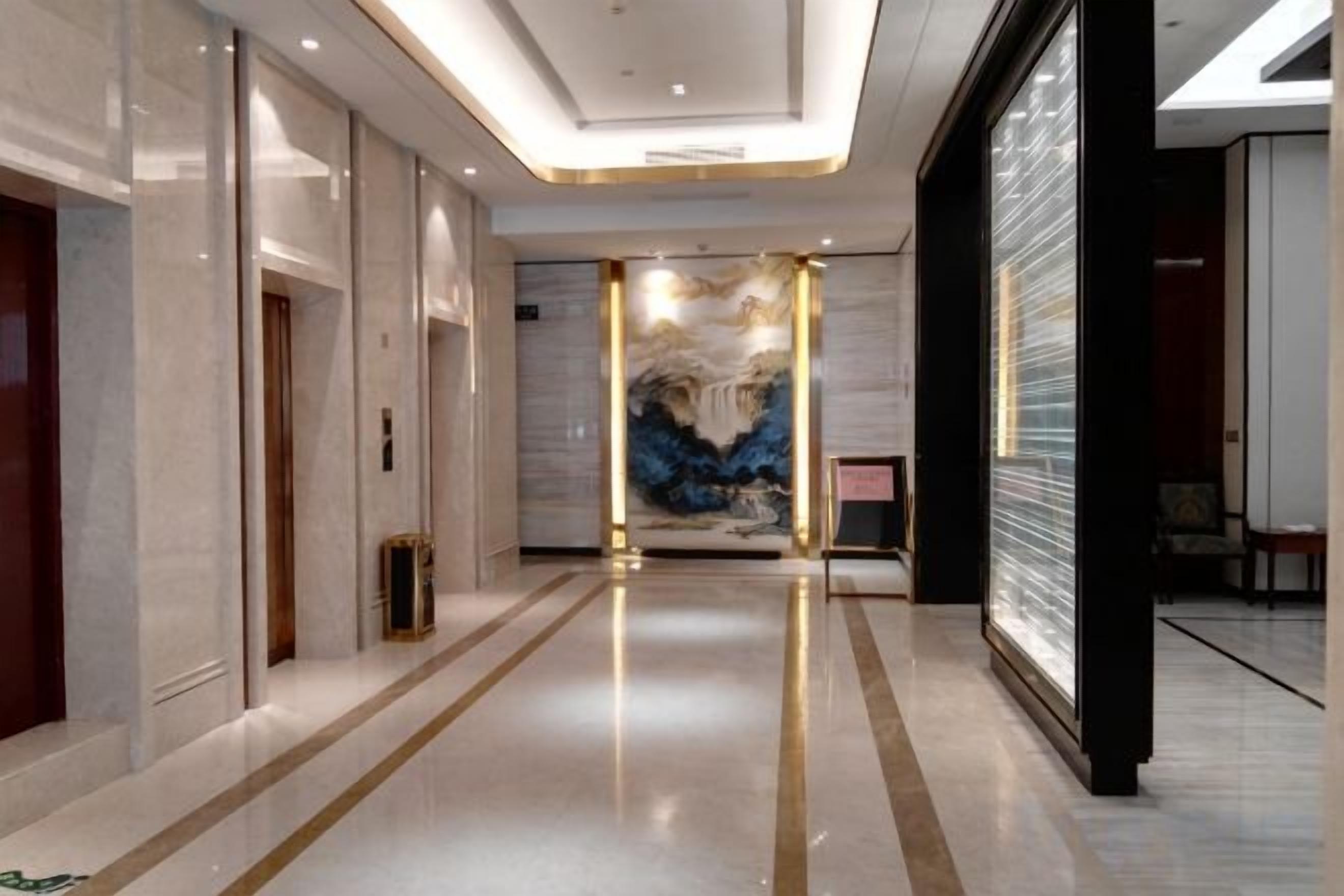 A hotel corridor with a polished floor, a reception desk, and a large abstract painting on the wall.