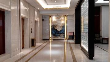 A hotel corridor with a polished floor, a reception desk, and a large abstract painting on the wall.