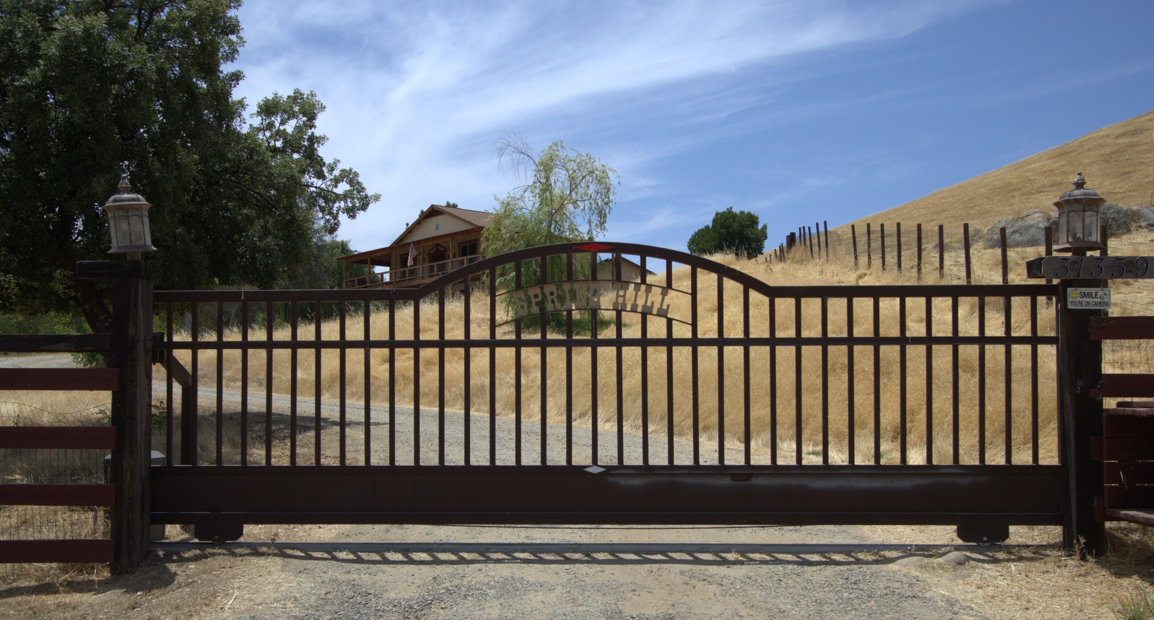 A gated entrance with a wooden fence, a house in the background, and a clear sky.
