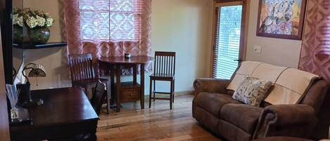 A living room with a brown leather sofa, a wooden coffee table, a dining table with chairs, and a patterned window.