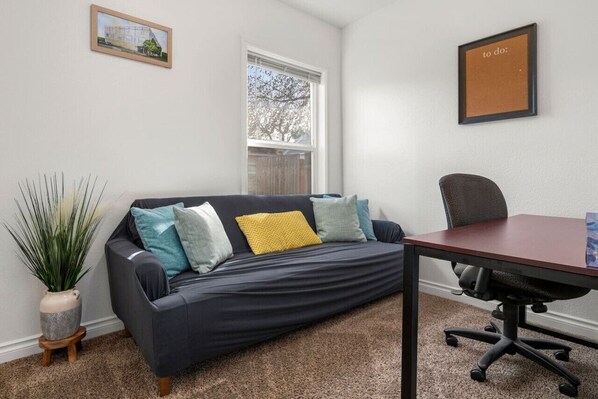 A room with a dark blue sofa, a wooden side table, a small potted plant, a framed picture on the wall, and a window with blinds.