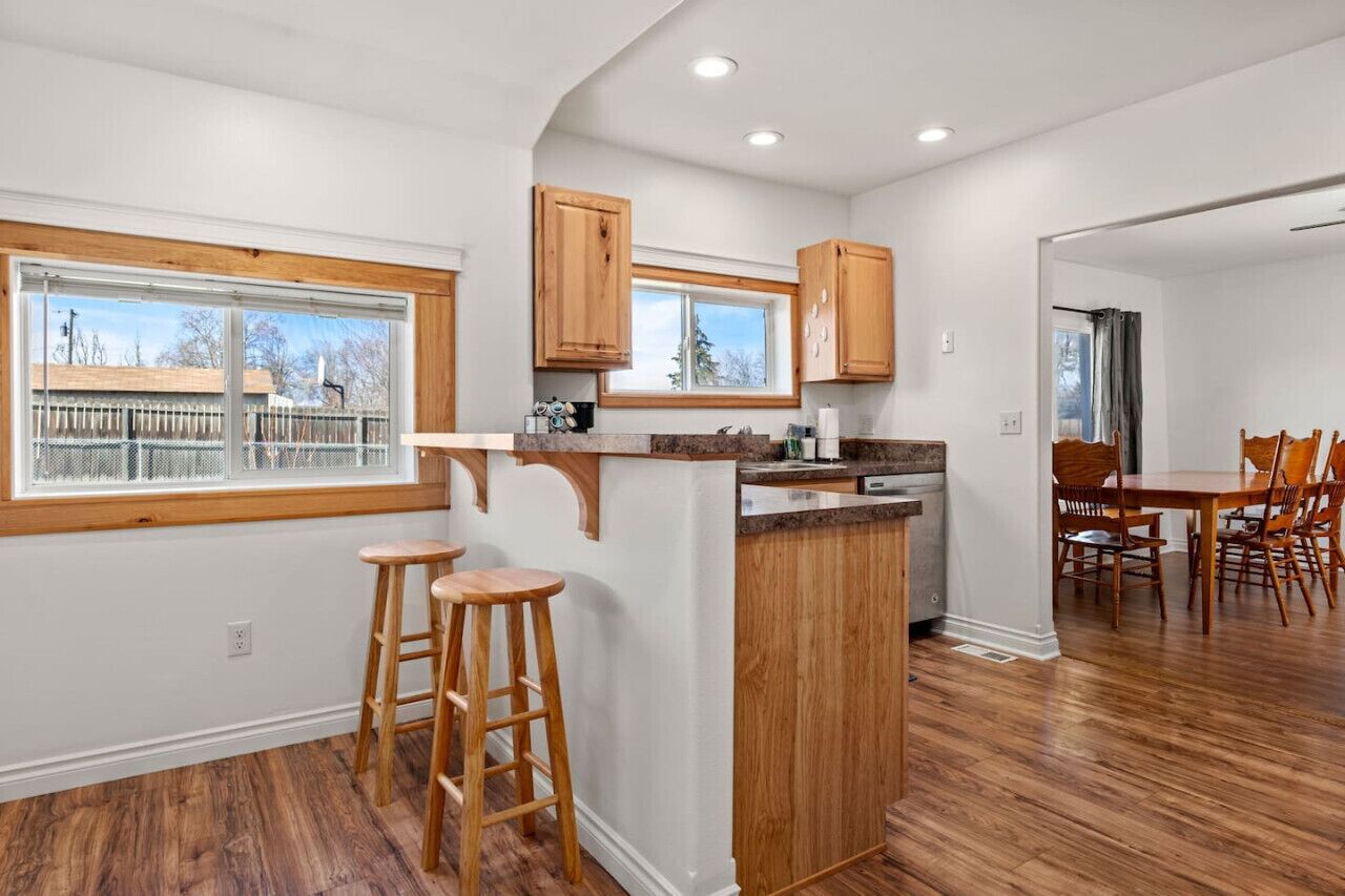 A modern kitchen with wooden cabinets, a bar stool area, and a dining table with chairs.
