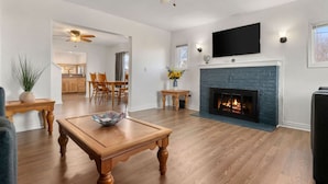 A spacious living room with hardwood flooring, a fireplace, a ceiling fan, and a television mounted above it. - Large Fenced Yard and Outdoor Patio (Lewiston)