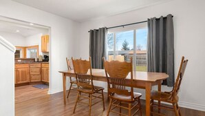 A dining area with a wooden table and four chairs, a window with curtains, and a view of a backyard. - Large Fenced Yard and Outdoor Patio (Lewiston)