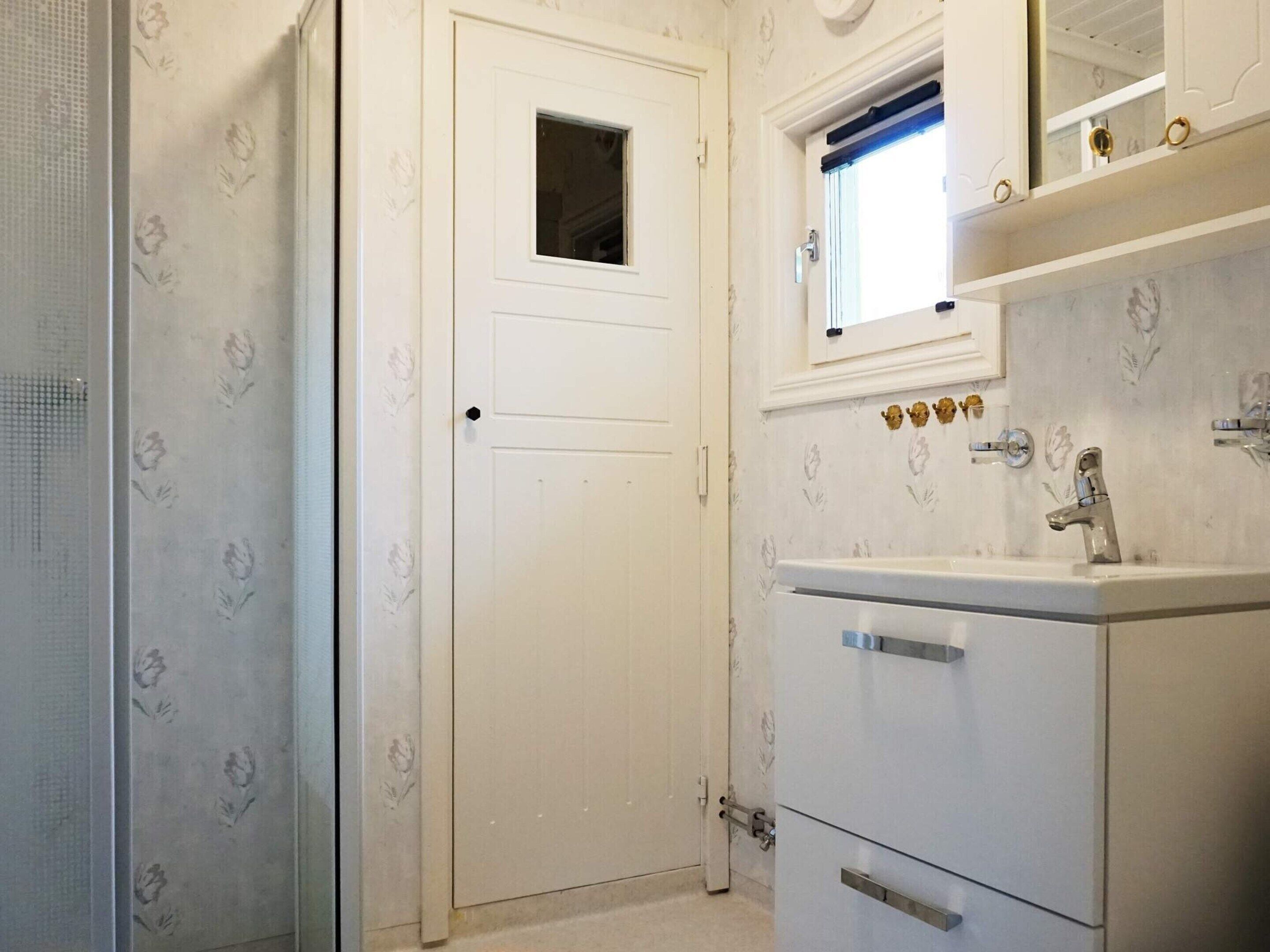 A bathroom with a white door, a window above the sink, and a mirror with decorative elements.