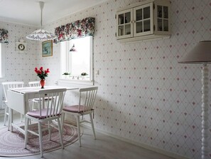 A dining area with a white table and chairs, a floral-patterned wallpaper, a window with curtains, and a clock on the wall. - 2 Person Holiday Home in Brastad-by Traum (Brastad)