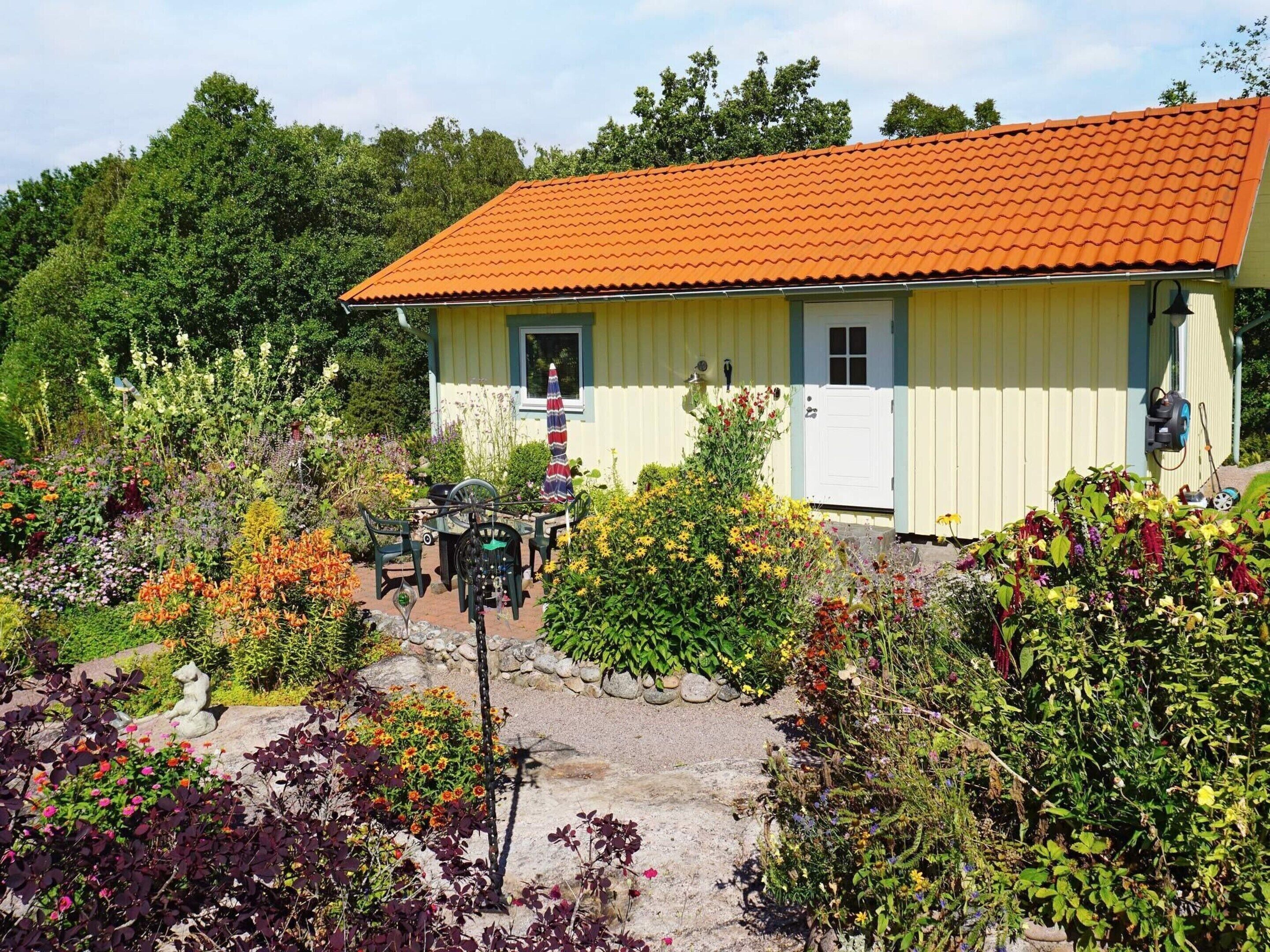 A yellow house with a red-tiled roof, surrounded by a garden with various plants and flowers.