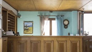 Ein Empfangsbereich mit Holztresen, einem Gemälde, einer Uhr und einem Fenster mit Vorhängen.