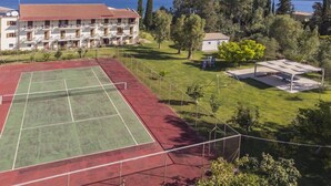 Ein Tennisplatz mit roter und grüner Belag, umzäunt, mit einem Gebäude im Hintergrund und Bäumen in der Nähe.