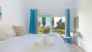 A hotel room with a large bed, a small stool, a mirror, and a view of the outdoors. - Sami Beach Hotel (Kefalonia)