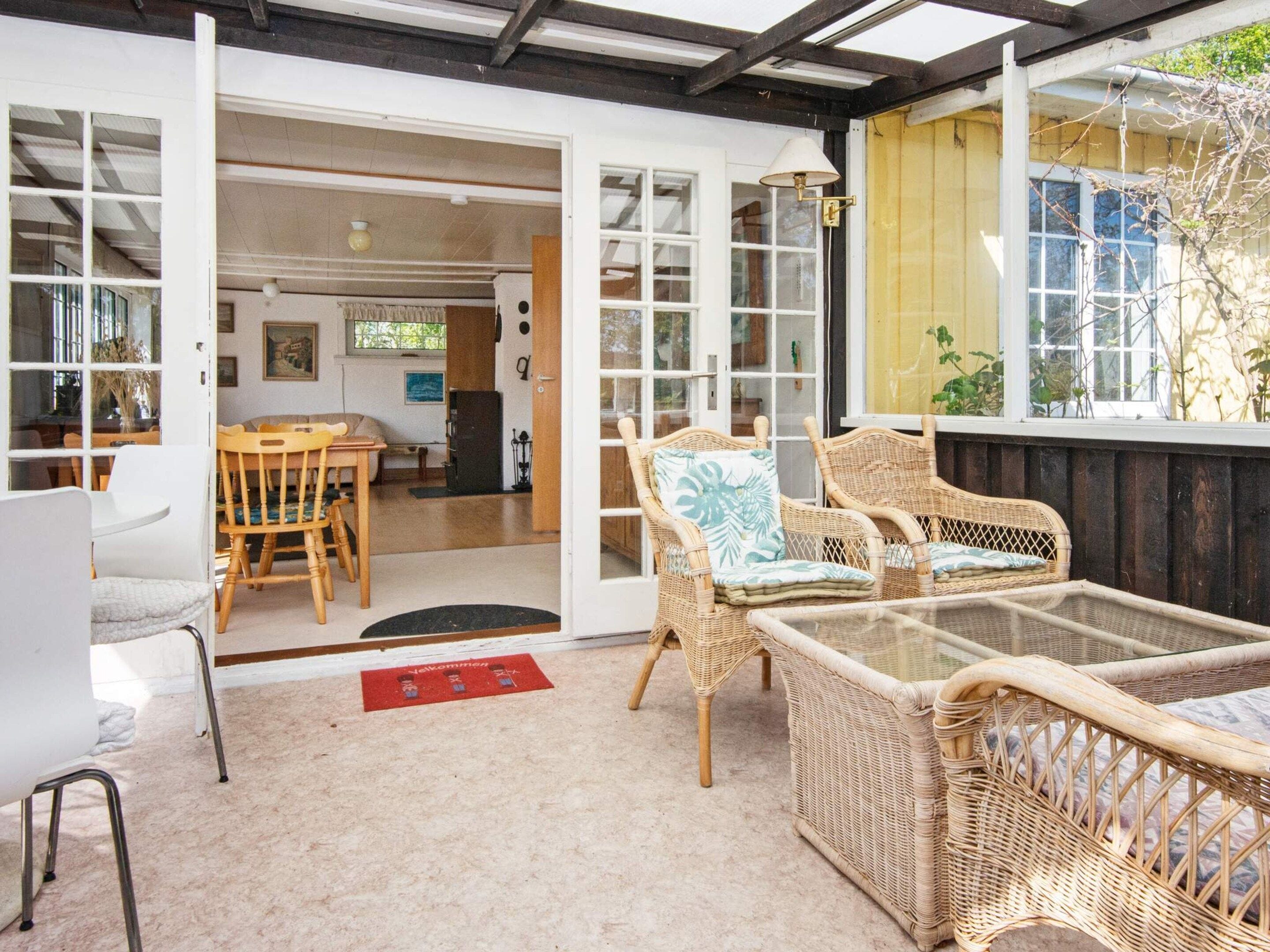 A room with wicker furniture, a glass table, and a red doormat.