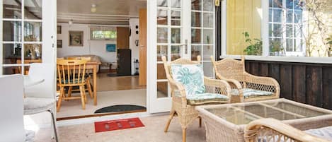 A room with wicker furniture, a glass table, and a red doormat.