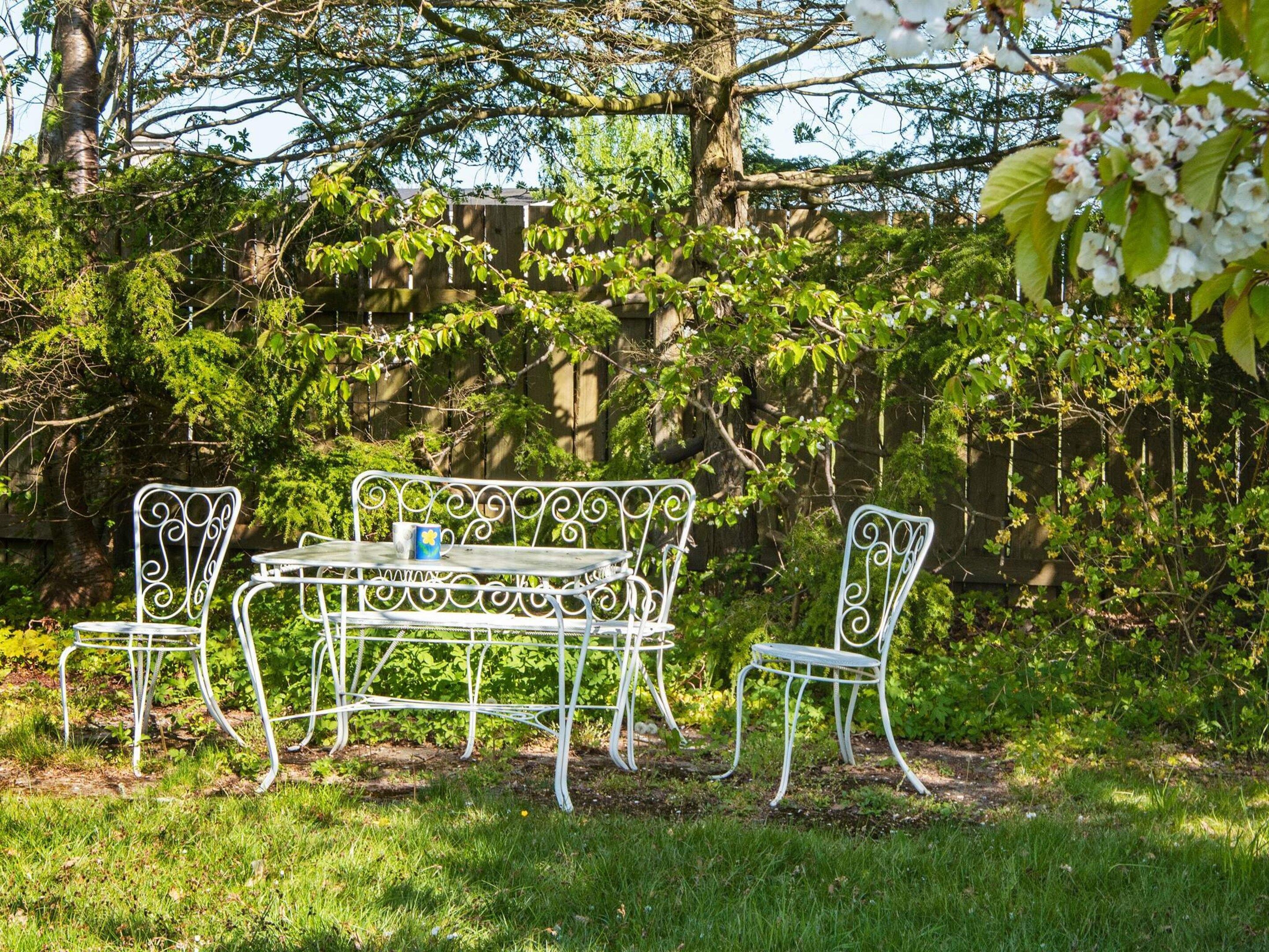 Un espace extérieur aménagé avec une table et des chaises en métal, entouré de verdure et d’arbres.