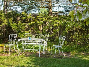 Un área de estar al aire libre con una mesa y sillas de metal, rodeada de follaje y árboles.