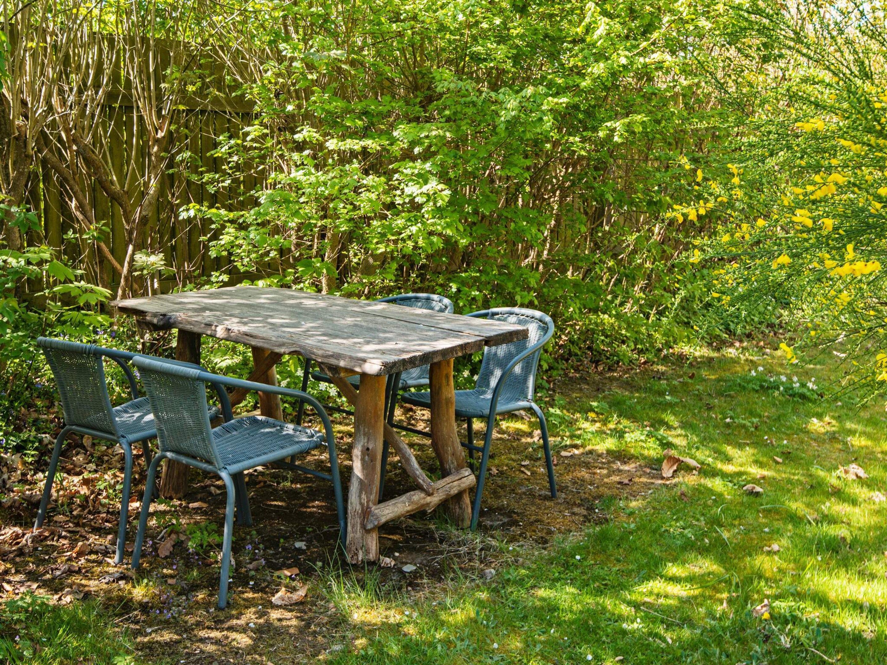 Een houten tuintafel met metalen stoelen in een tuin.