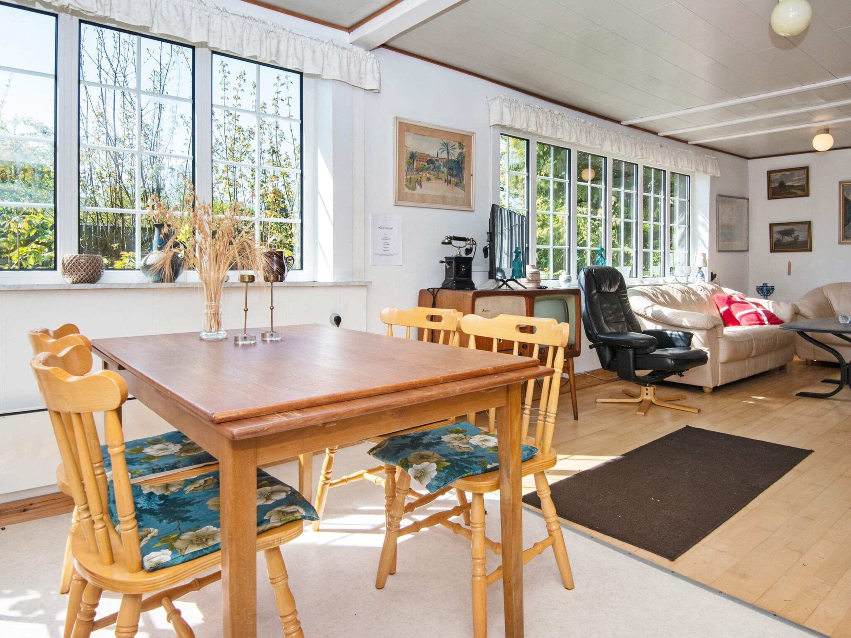 A room with a wooden dining table, chairs, a sofa, and a television.
