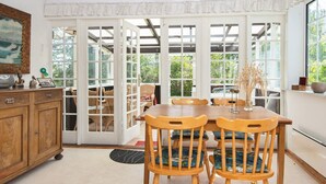 Uma sala de jantar com uma mesa e cadeiras de madeira, um armário e vista através de grandes portas de vidro.