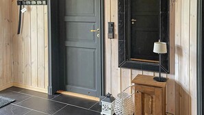 A wooden interior with a dark grey door, a small wooden cabinet, and a white wicker basket. - 4 Star Holiday Home in Veggli (Rollag)
