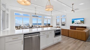 A spacious kitchen with a large island, white cabinetry, stainless steel appliances, and a view of the ocean.