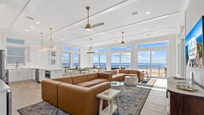 A spacious living area with a large brown sectional sofa, a small round coffee table, and a view of the ocean through large windows.