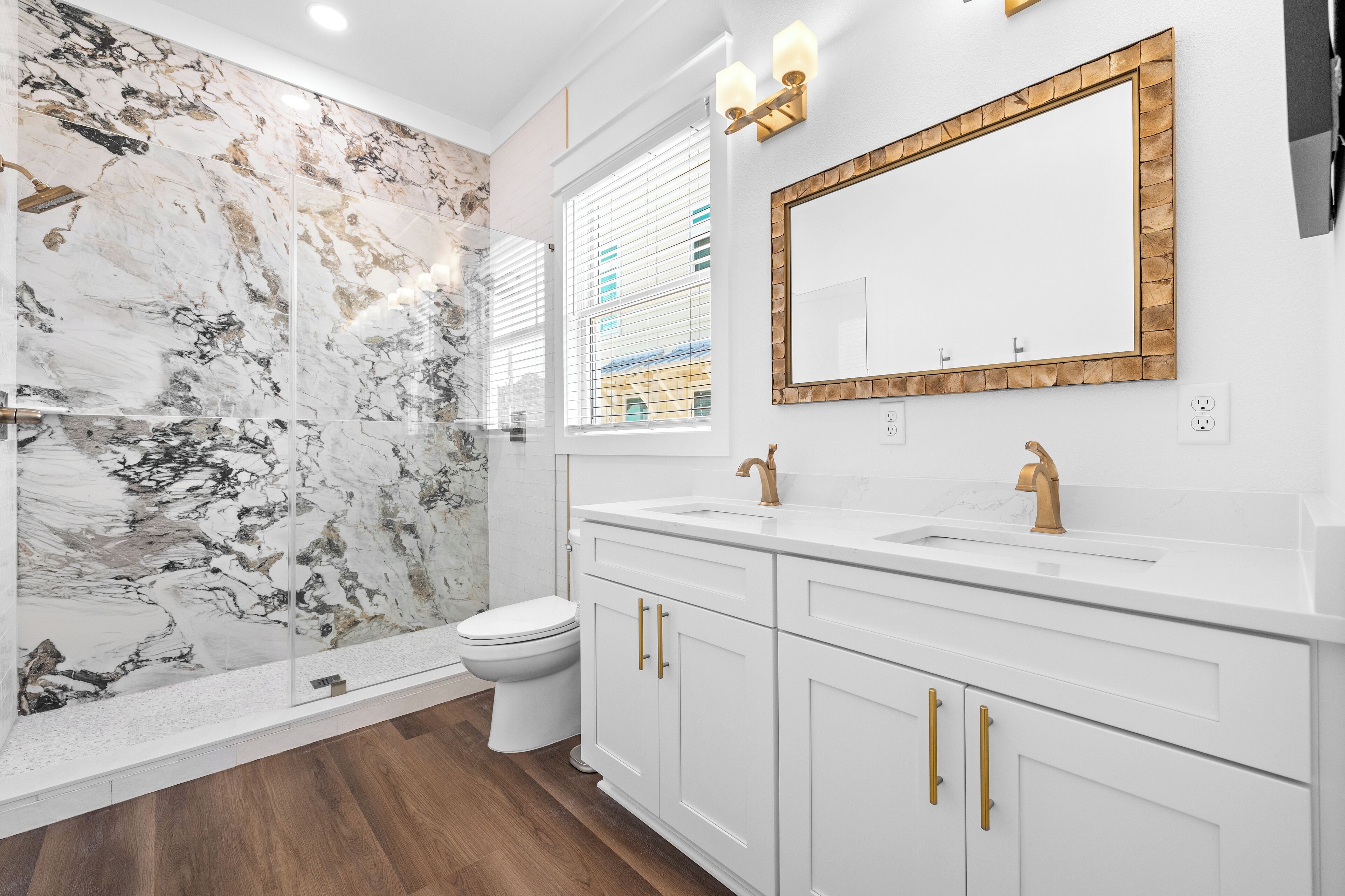 A modern bathroom with a marble wall, white vanity, gold fixtures, and a large mirror.