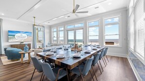 A spacious dining area with a long wooden table set for six, surrounded by blue chairs. - Silver Strand: Large 7 BR Beachfront Home- Sleeps 24, Pet Friendly, Priv. Pool (Indian Pass)
