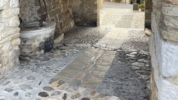 An arched stone corridor with a cobblestone floor, a hanging lantern, and a sign indicating a room named "ROOMA ATELIER".