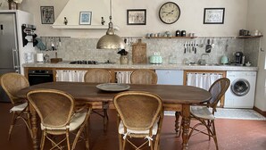 A kitchen with a dining table, wicker chairs, a large pendant light, and a washing machine.