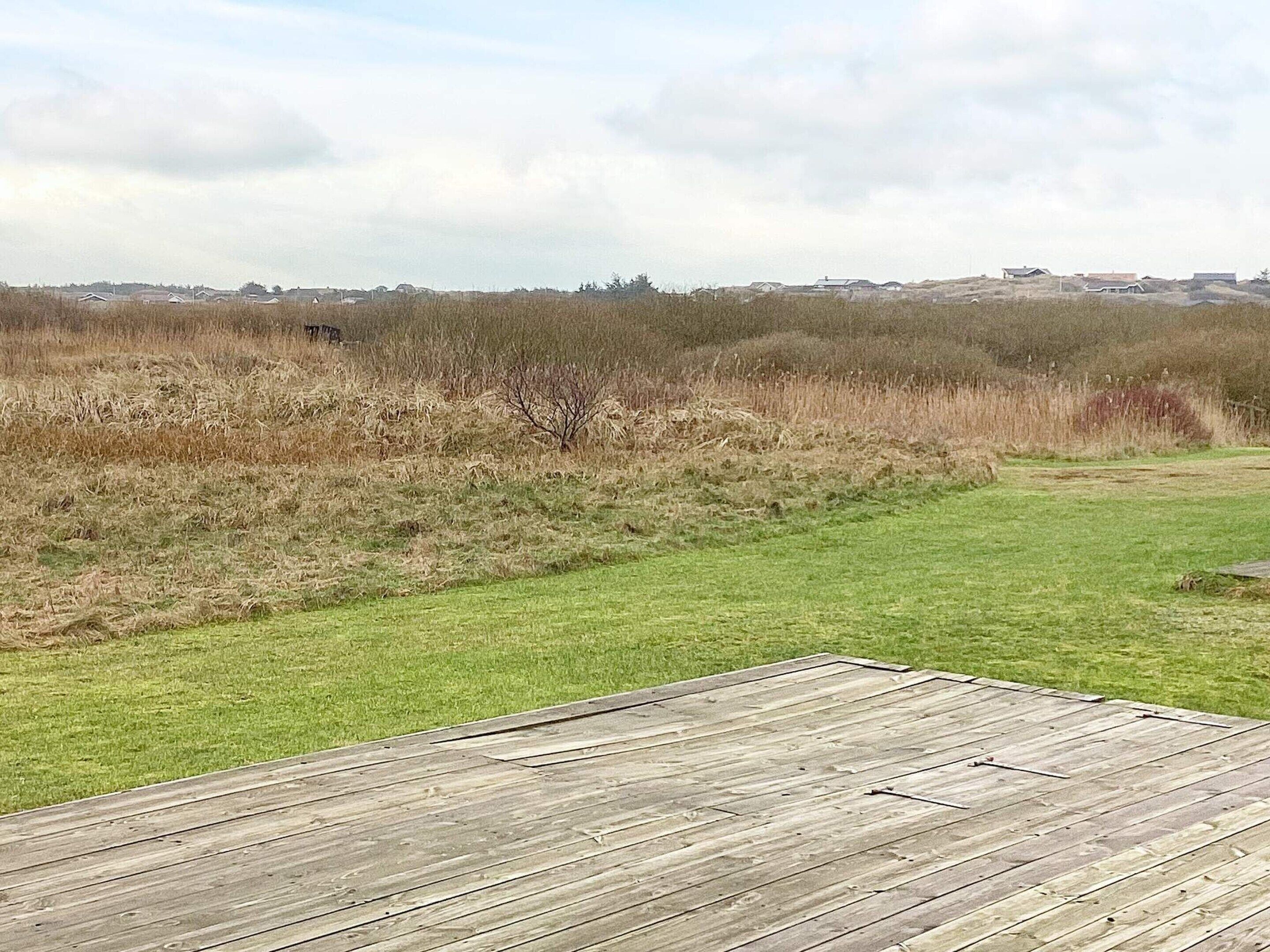A wooden deck with a grassy area in the foreground and a field with sparse vegetation in the background.