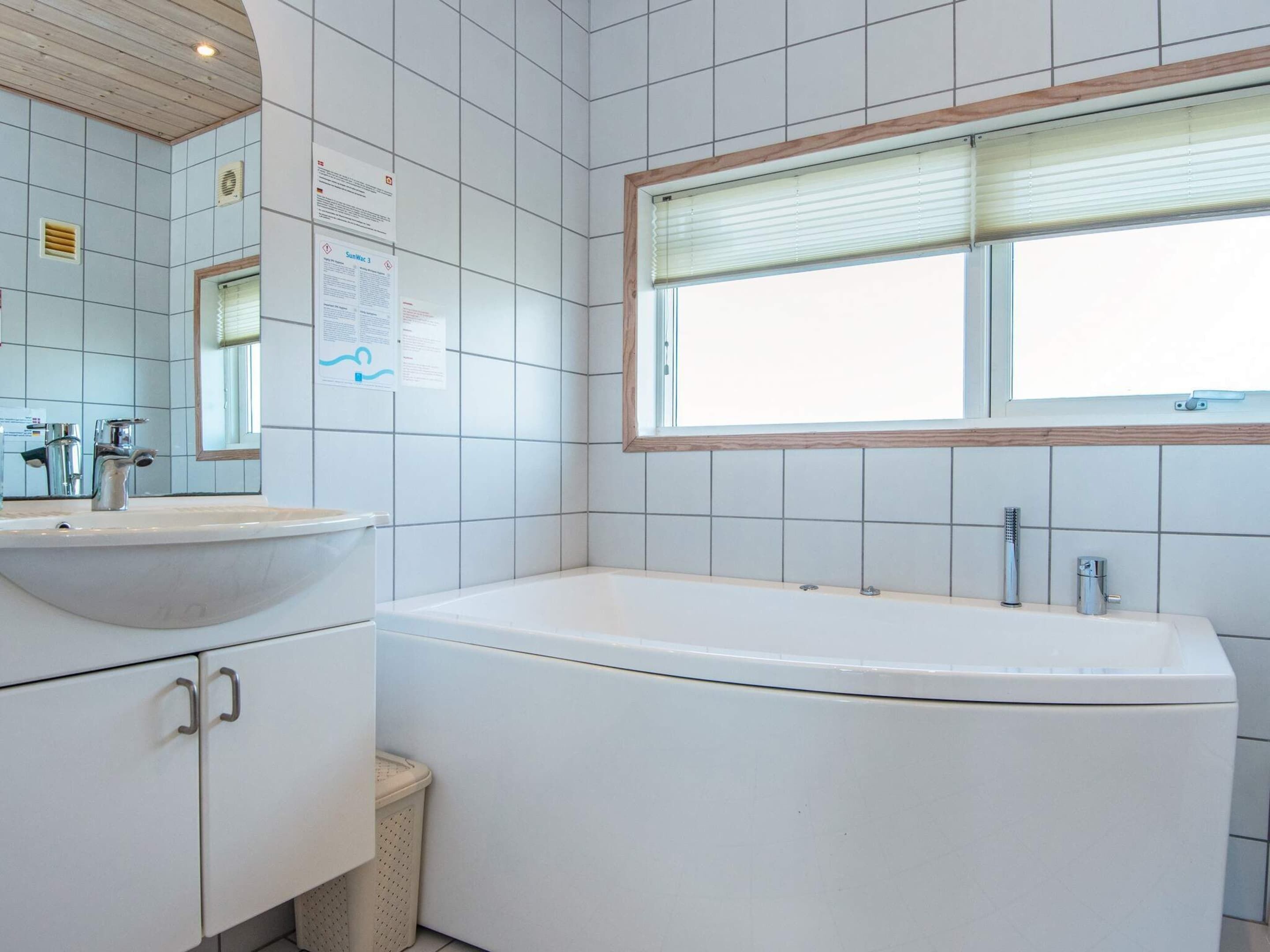 Une salle de bain moderne avec une baignoire sur pieds, un lavabo avec un miroir et une fenêtre avec des stores.