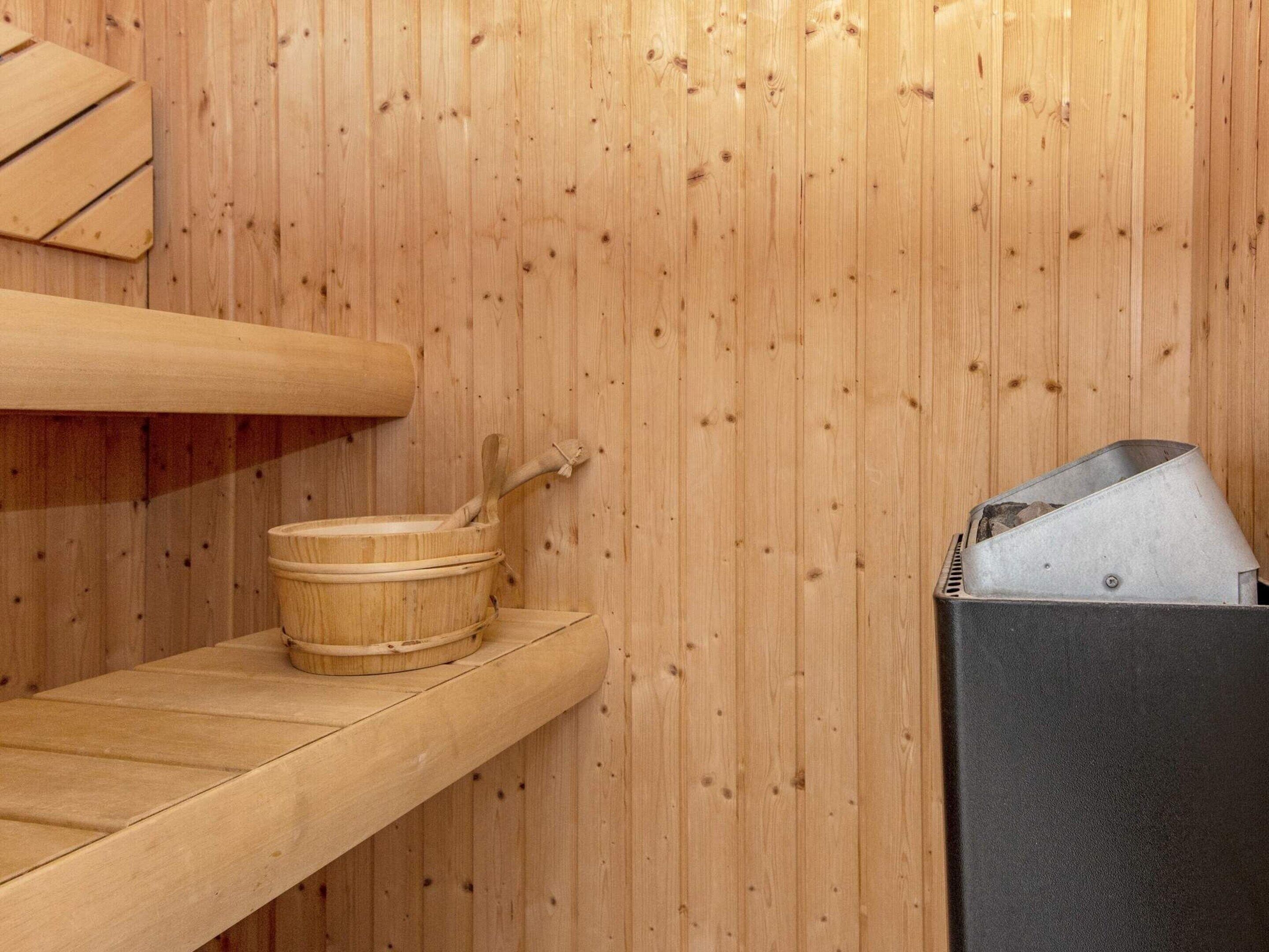A wooden sauna with a wooden bench, a wooden bucket, and a metal container.