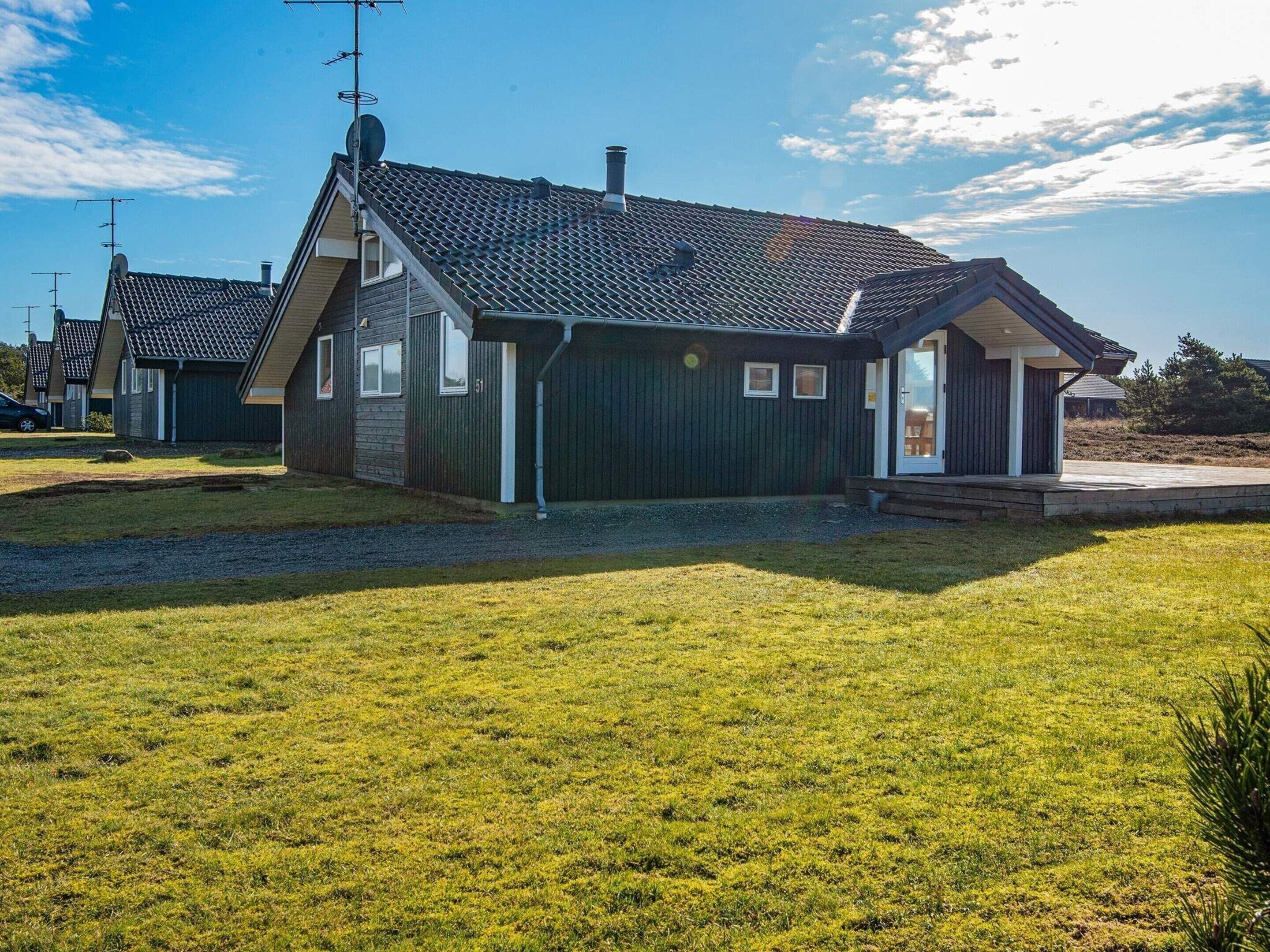 Une maison de plain-pied à l’extérieur vert foncé, avec un toit en tuiles et un petit porche.
