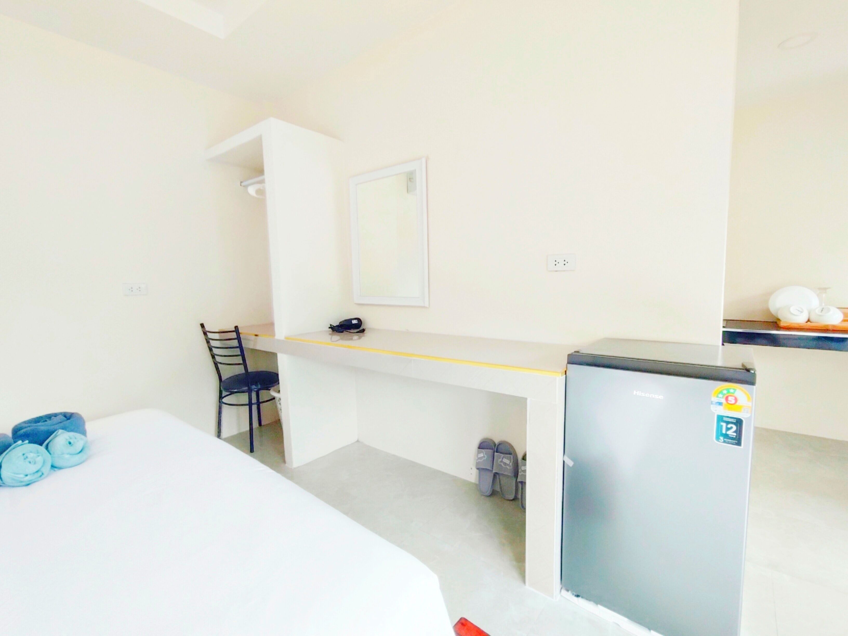 A small, clean room with a bed, a desk, a chair, a refrigerator, and a mirror.