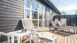 A wooden deck with white furniture, including a table and chairs, and a covered area with lounge chairs. - 12 Person Holiday Home in Albaek (Aalbaek)