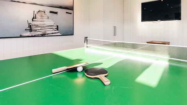 A ping pong table with paddles and a ball, a painting of a pier, and a TV on the wall. - 12 Person Holiday Home in Albaek (Aalbaek)