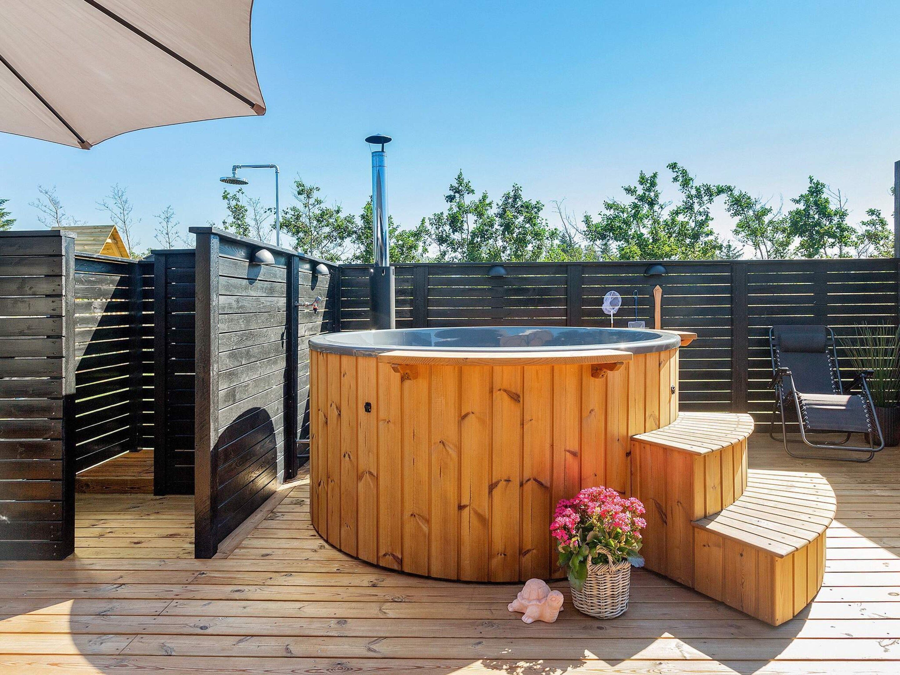 Una bañera de hidromasaje de madera con una terraza también de madera, una mesita y una silla.