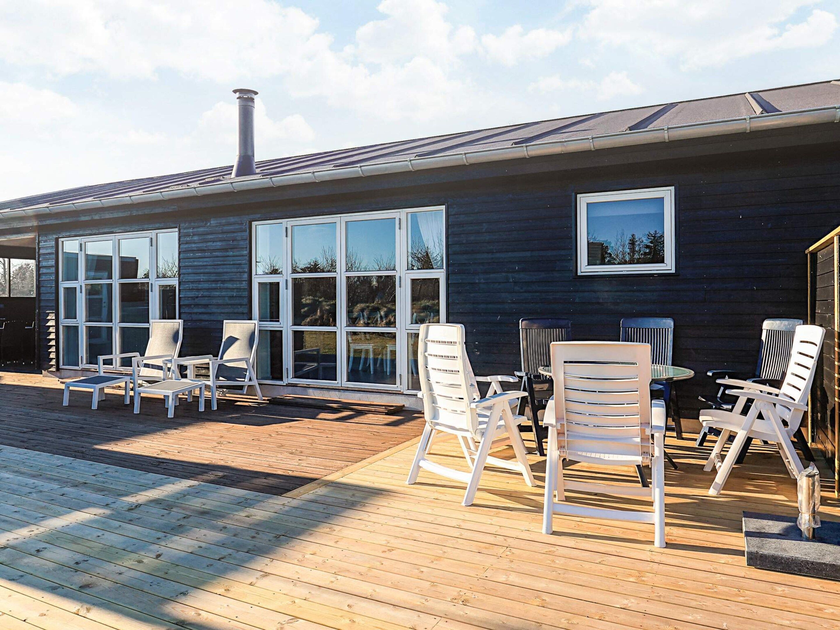 Et moderne hus med terrasse, store vinduer og udendørs møbler.