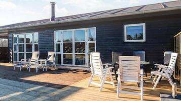 Et moderne hus med terrasse, store vinduer og udendørs møbler.