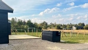 A building with a dark exterior, a fenced area with a wooden structure, and a clear sky. - 12 Person Holiday Home in Albaek (Aalbaek)