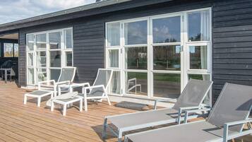 En terrasse med liggestole, grill og store vinduer.