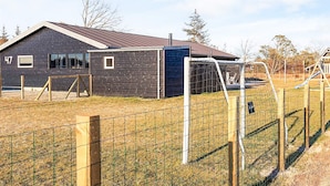 A modern building with a dark exterior, numbered 47, and a fenced area with playground equipment. - 12 Person Holiday Home in Albaek (Aalbaek)