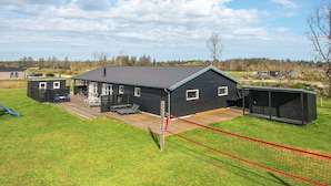 A black building with a flat roof, a deck, and a fenced area with lounge chairs. - 12 Person Holiday Home in Albaek (Aalbaek)