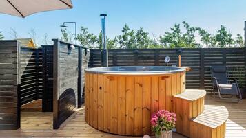 En træterrasse med jacuzzi, siddepladser og et træhegn.