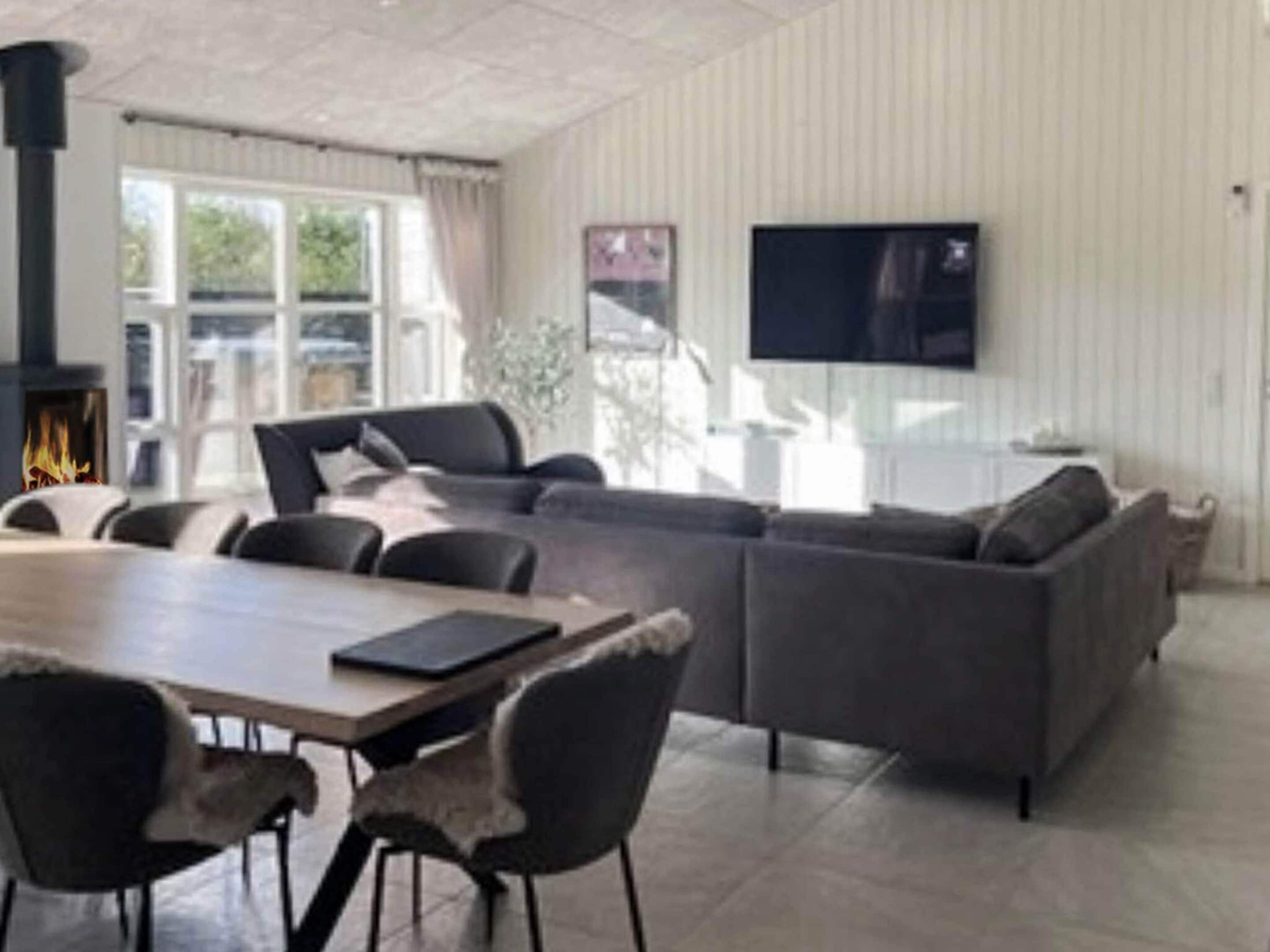 En moderne stue med sofa, stole, spisebord, pejs og et fjernsyn monteret på væggen.
