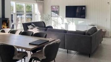 En moderne stue med sofa, stole, spisebord, pejs og et fjernsyn monteret på væggen.