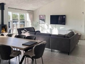 A modern living room with a sofa, chairs, a dining table, a fireplace, and a TV mounted on the wall. - 12 Person Holiday Home in Albaek (Aalbaek)