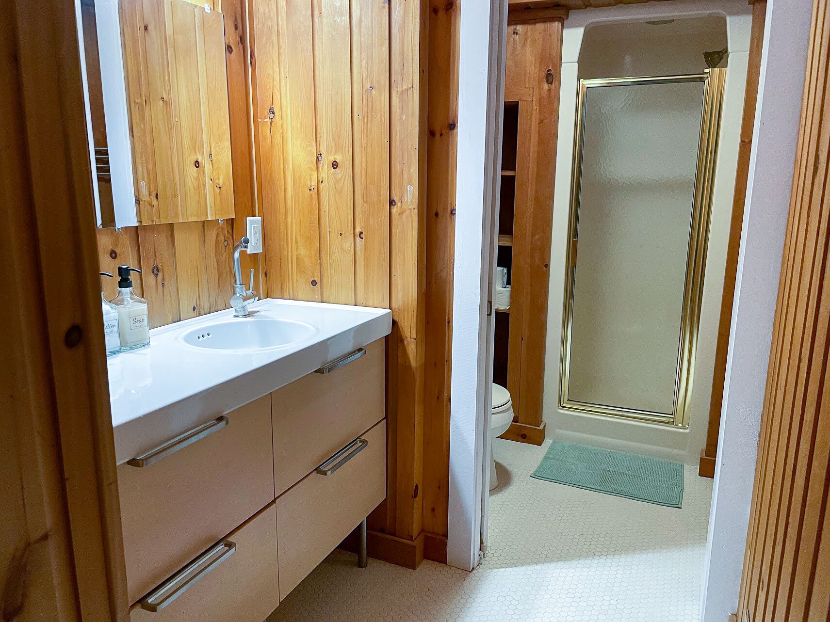 A bathroom with wooden paneling, a white sink, and a glass shower enclosure.