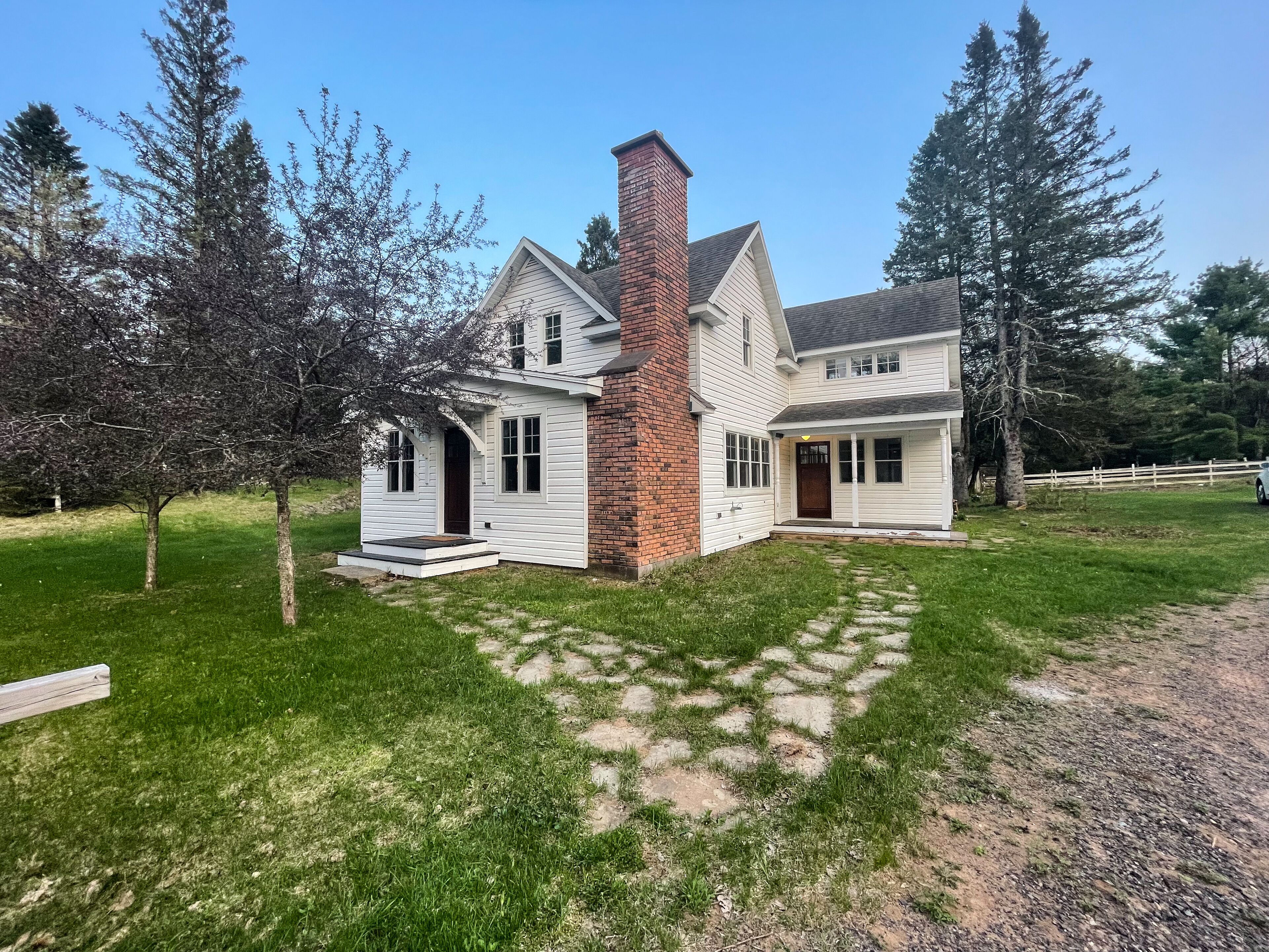 A two-story house with a brick chimney, white siding, and a front porch.