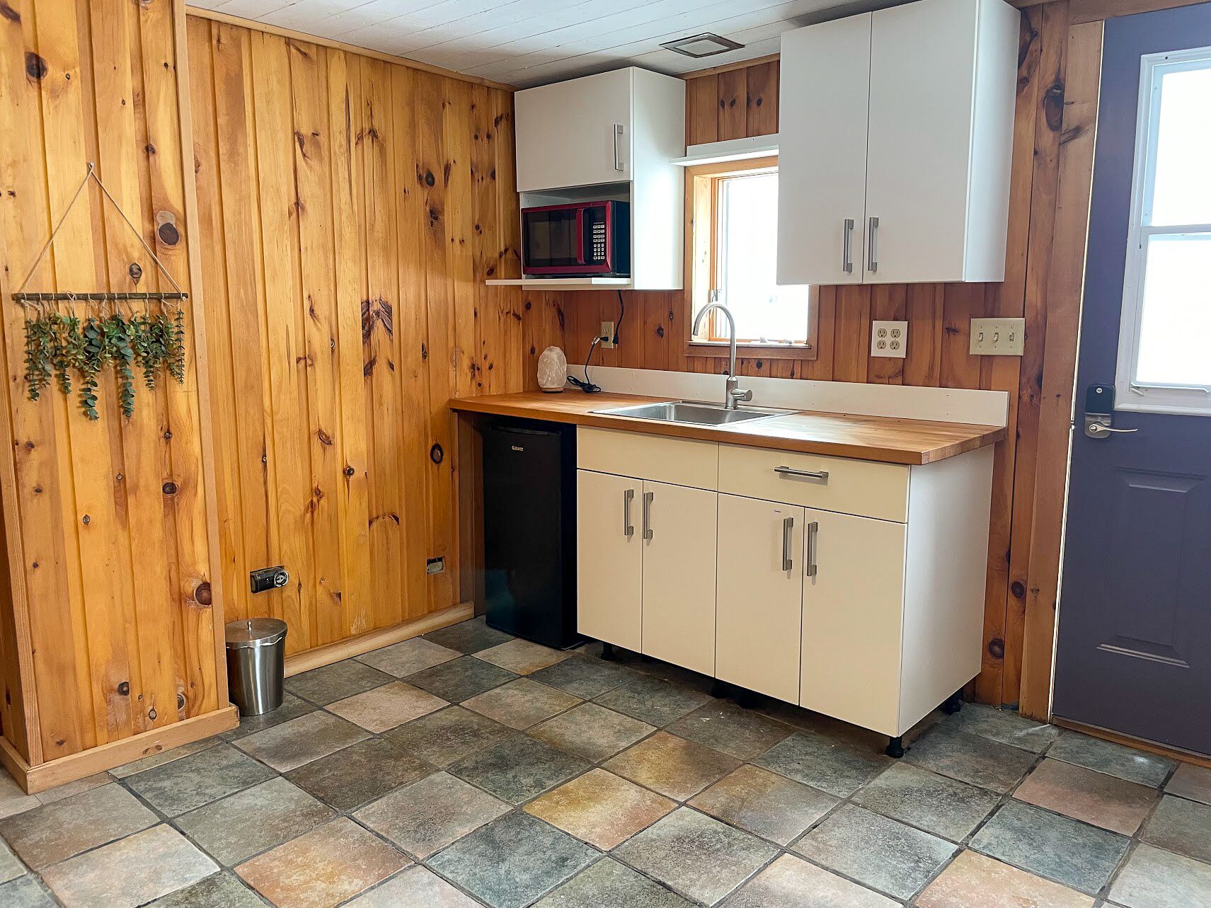 A compact kitchen with wooden walls, a dishwasher, a microwave, and a sink.