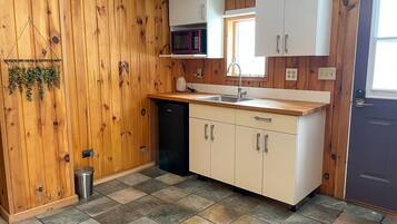 A compact kitchen with wooden walls, a dishwasher, a microwave, and a sink.
